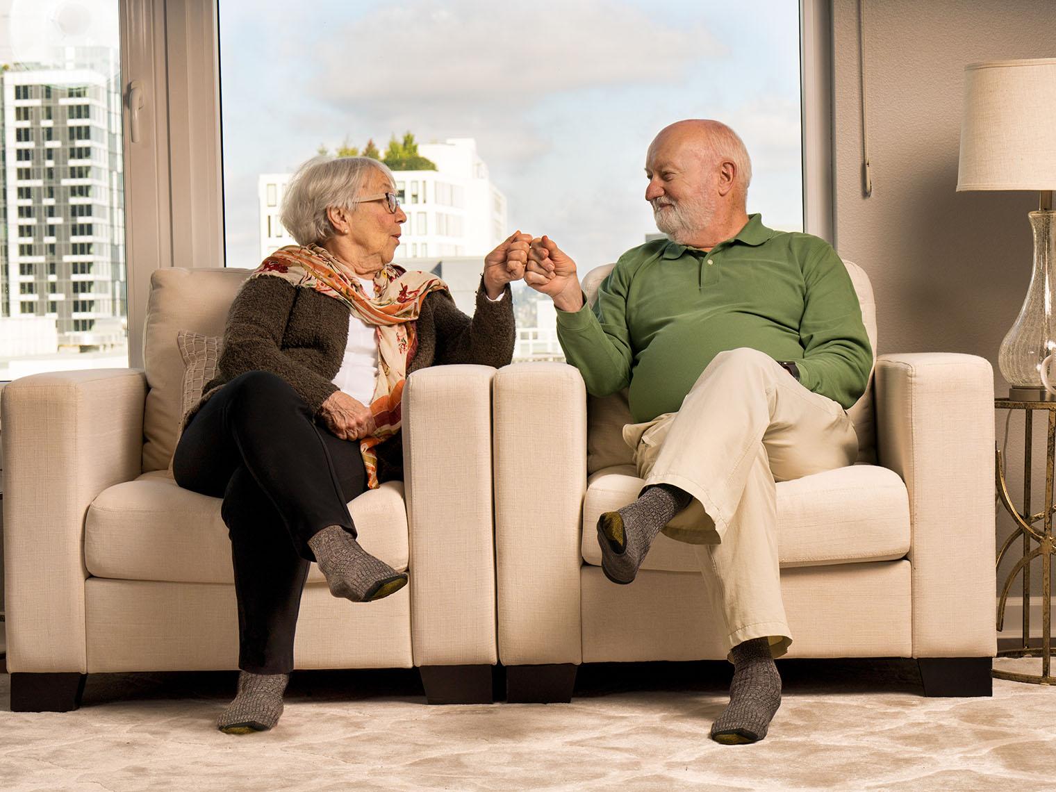 A senior couple sits together holding hands in luxury accomodations.